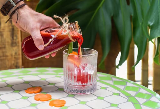 Hand pouring healthy mixed juice made of carrot, orange fruit, pink dragon fruit, apple with glass with ice