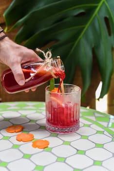 Hand pouring healthy mixed juice made of carrot, orange fruit, pink dragon fruit, apple with glass with ice