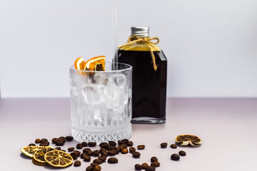 Cold brew coffee in a bottle with transparent glass full of ice on light gray background