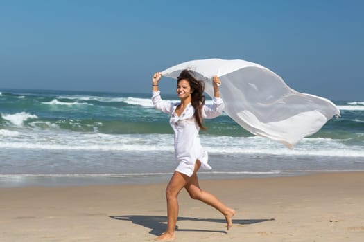 Beautiful young woman relaxing at the beach and holding a white fabric