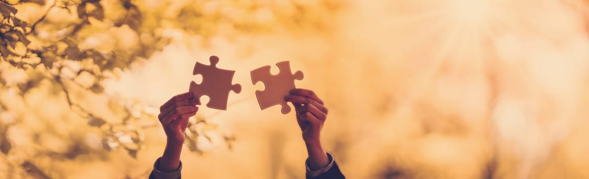 Silhouette of the human hand with piece of jigsaw outdoors on the nature background. Concept of the teamwork and togetherness