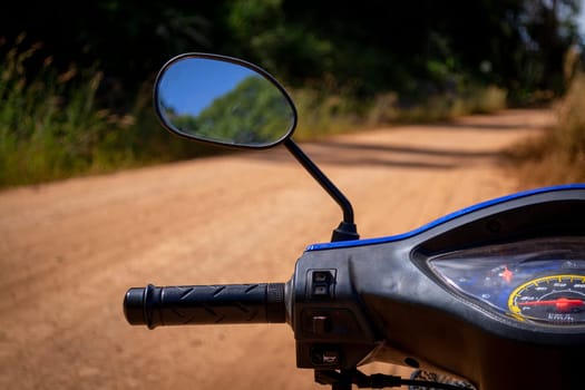 Small motorbike or scooter dashboard with dirt track leading into nature. Out of focus background.