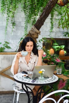 Young ukrainian brunette woman freelancer working with laptop and drinking coffee in cafe