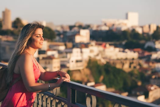 Young woman tourist enjoying beautiful landscape view on the old town with river and famous iron bridge during the sunset in Porto city, Portugal