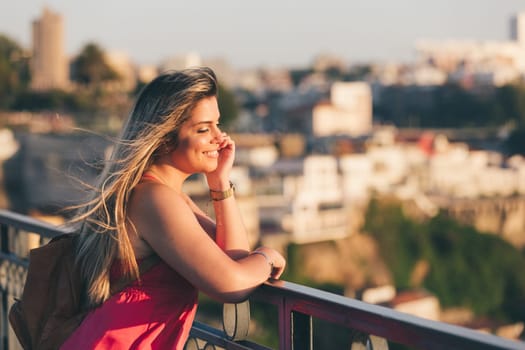 Young woman tourist enjoying beautiful landscape view on the old town with river and famous iron bridge during the sunset in Porto city, Portugal