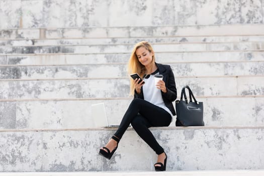 Young attractive businesswoman sitting on the stairs and using modern laptop