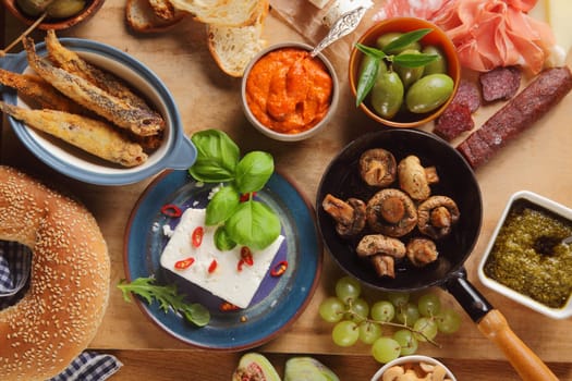 Close up Assorted Tapas Foods on Wooden Table, Emphasizing Cheese, Mushrooms, Meats, Bread, Olives and Sauce.