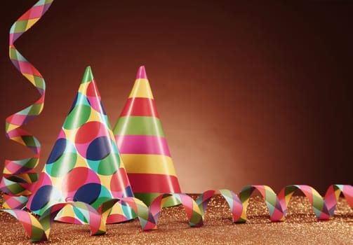 Close up Party Carnival Hats with Different Designs and Paper Streamers on Top of the Table, with Particles, in front Gradient Brown Background.