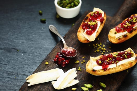 Gourmet open sandwiches on grilled rolls with camembert cheese and cranberry preserve sprinkled with chopped pistachios, high angle with copyspace