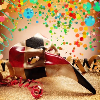 Close up Festival Venetian Masquerade Mask with Long Beak on Top of Glittery Table with Paper Streamer, Styled with Colorful Abstract Festival Designs with Gradient Brown Background.