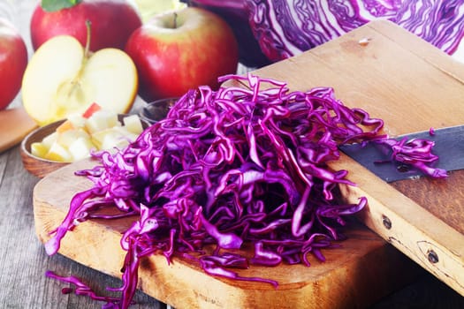 Close up Fresh Shredded Purple Cabbage on Wooden Chopping Board on Top of Wooden Table with Other Fresh Ingredients.