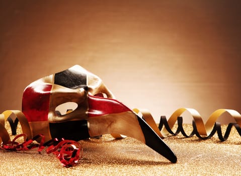 Close up Venetian Masquerade Mask with Streamers on Glittery Table In front Gradient Brown Background. Emphasizing Copy Space.
