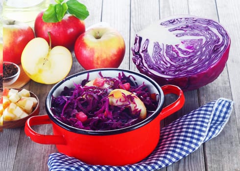 Close up Appetizing Healthy Purple Cabbage and Apple Salad Recipe on Red Pot, Placed on the Table with Cloth and Other Fresh Ingredients.