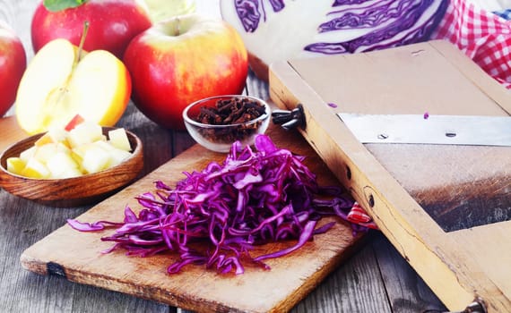 Close up Thin Slices of Fresh Purple Cabbage for Salad on Wooden Chopping Board on Top of Wooden Table with Other Fresh Ingredients.