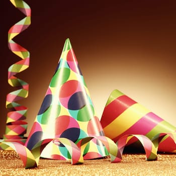 Close up Carnival Hats and Paper Streamers on Platform with Golden Particles in front Gradient Brown Background.