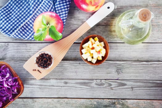 Aerial Shot of Salad Recipe Ingredients on Top of Wooden Table, Emphasizing Apples, Cabbage and Vinegar with Napkin and Wooden Ladle.