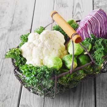Wire basket of farm fresh cruciferous vegetables with a cauliflower, red cabbage, brussels sprouts and leafy green kale on rustic grey wooden boards