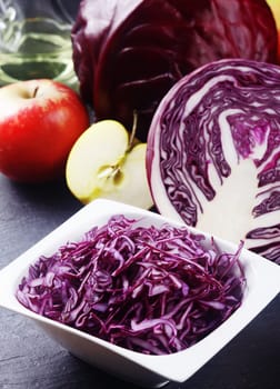 Close up Shredded Purple Cabbage on White Bowl on Top of the Table with Apples and Other Cabbage.