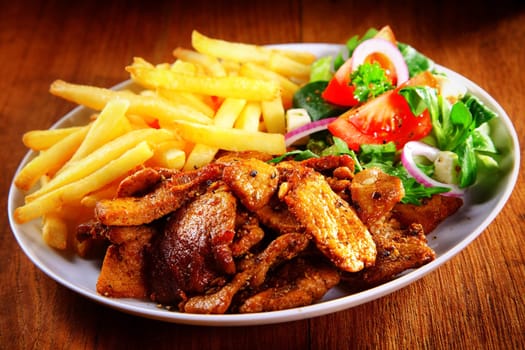 Close up Appetizing Healthy Meal Combination of Cooked Meat, French Fries and Fresh Veggies on Top of Brown Wooden Table.