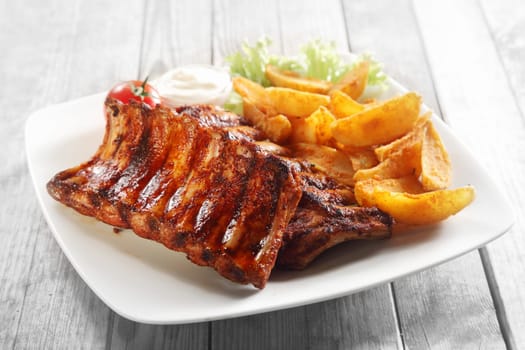 Close up Gourmet Main Dish with Grilled Pork Rib and Fried Potatoes on White Plate. Served on Wooden Table.