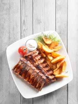 Close up Aerial Shot of Grilled Pork Rib Meat, Crispy Fried Potatoes with Sauce on White Plate. Placed on Gray Wooden Table.