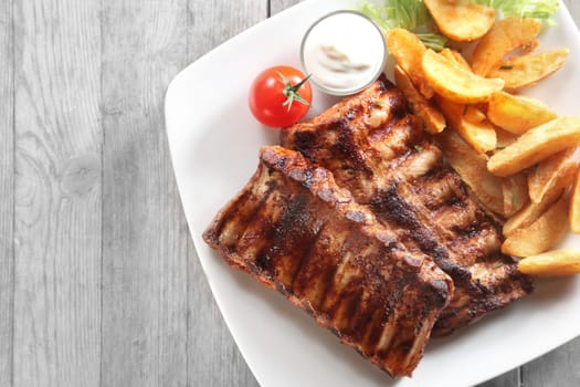Close up Tasty Grilled Pork Rib and Fried Potatoes on White Plate with White Sauce on a Plate. Placed on Wooden Table With Copy Space.