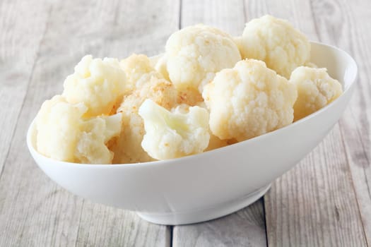 Bowl of healthy fresh steamed or microwaved white cauliflower broken into florets and served on a rustic grey wooden table, tilted angle close up view