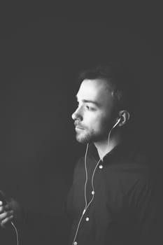 Man listening to music on an MP3 player standing holding the device in his hand listening to the tunes over earplugs, greyscale image with copyspace