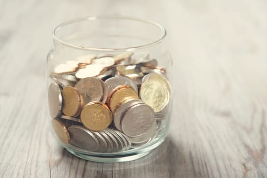Coins in glass money jar, on wooden background.