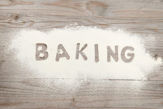 Word baking written in white flour on a old wooden table, low light vintage tone.