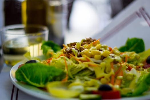 Vegetarian plate with vegetables, mais, salad and nuts, glass of white wine in the background. Food and drink.