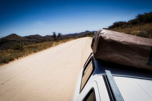 Dirt or gravel road view of 4x4 truck with folded rooftop tent during a safari trip in Africa. Travel and tourism.