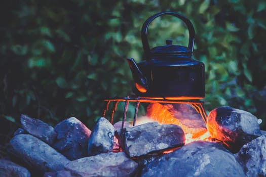 Adventure cooking during camping: metal kettle boiling on a campfire, surrounded by stones. Back to basics. Copy space provided.