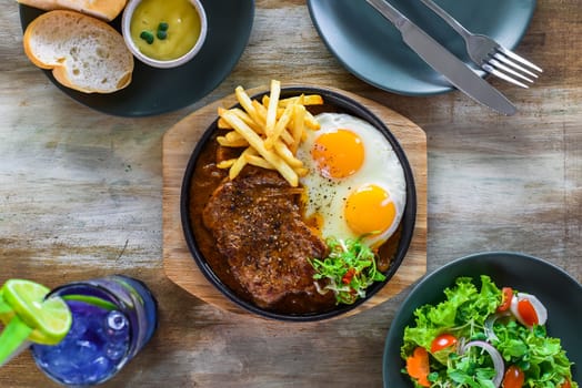 Vietnamese beef steak with french fries, fried eggs, baguette, served with lemonade drink, vegetable salad