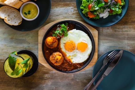 Vietnamese Banh mi chao dish with salted egg yolk meatballs, tomatoes relish, fried eggs and served with sauce, salad and lemonade drink