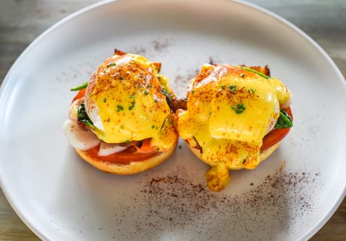 English muffin with poached eggs, bacon and Hollandaise sauce with vegetables
