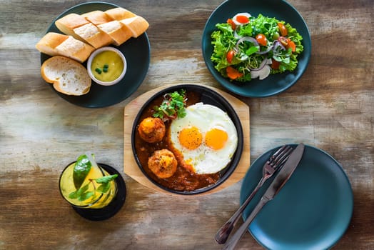 Vietnamese Banh mi chao dish with salted egg yolk meatballs, tomatoes relish, fried eggs and served with sauce, salad and lemonade drink