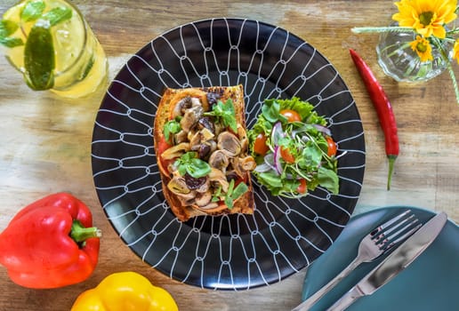 Mushrooms on toast with hummus, garlic butter, thyme and truffle oil on wooden table with fork, knife and lemonade drink