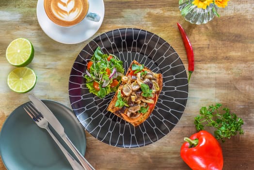 Mushrooms on toast with hummus, garlic butter, thyme and truffle oil on wooden table with fork, knife and lemonade drink