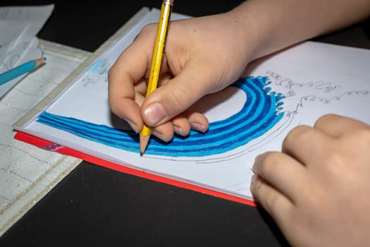 Hand with pen of a child who is sitting at a table and drawing a picture.