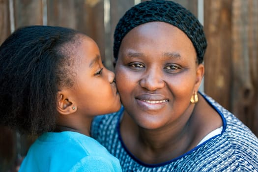 Close up portrait of little girl kissing mother on cheek outdoors.
