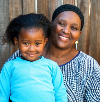Portrait of african mom and daughter against wooden fence.