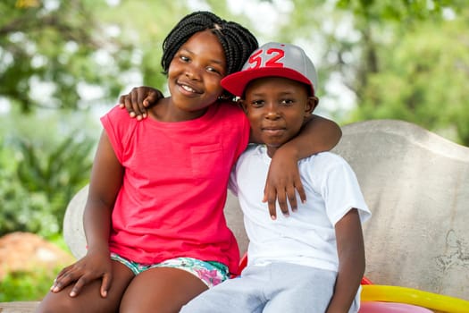 Close up portrait of two African kids sitting together on bench in park.