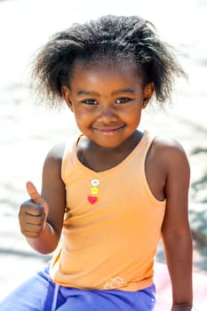 Outdoor portrait of cute African girl doing thumbs up sign.