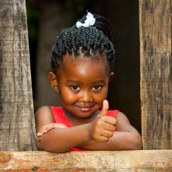 Portrait of small african girl doing thumbs up at wooden fence.