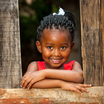 Close up portrait of pretty african youngster leaning on wooden fence outdoors.