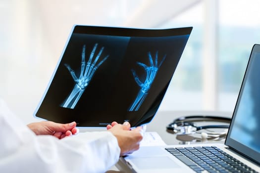 Close up of Female doctor at desk with laptop holding and reviewing trauma x-ray.