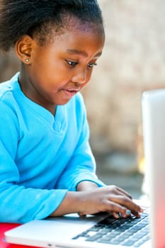 African girl typing and navigating on laptop outdoors.