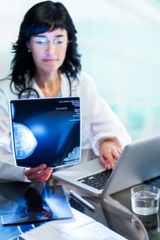 Close up portrait of Female doctor analyzing x-ray mammogram at desk in clinic.