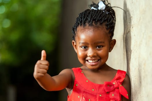 Portrait of happy little african girl doing thumbs up sign outdoors.